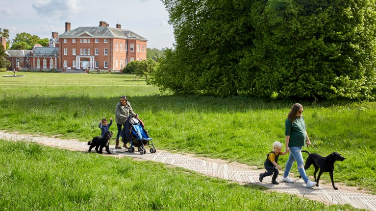Visitors walking dogs in the grounds at Hatchlands Park, Surrey
